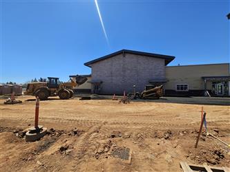 a view of the multipurpose room from the dirt parking area with heavy equipment working on the grounds