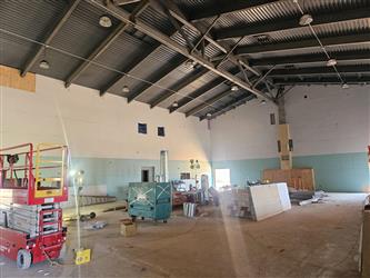 the interior of the multipurpose room with new drywall installed on the walls and an exposed metal roof with hanging light fixtures