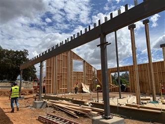 Steel supports holding a steel beam in the middle of a new classroom building with some walls framed.