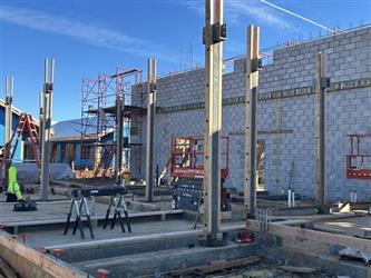 steel beams erected from the ground with a concrete block wall in the background
