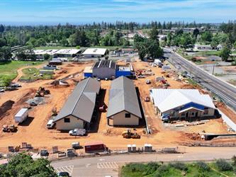 a high drone shot pointing West showing many dirt paths across the property and the 4 buildings under construction