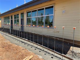 a row of rebar for a future retaining wall and classroom in the background with siding and windows complete