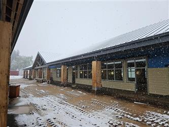 a large classroom building under construction with partial siding and metal roof in heavy falling snow