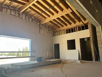The interior exposed wood rafters over the stage in the multipurpose room with drywall on some walls.