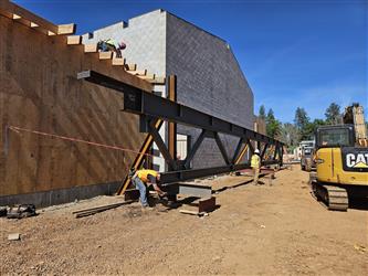 A large CMU block building with wood framed walls extending out and a large steel truss sitting on the ground