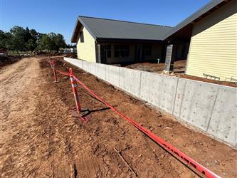 a long concrete wall with two exterior buildings covered in unpainted siding and metal roofing