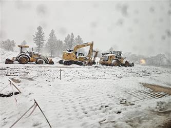 several large earth moving vehicles in heavy falling snow in an open field