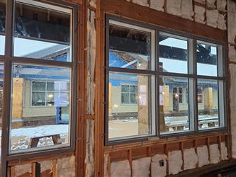 interior building under construction with framing and insulation and windows looking outside to falling snow