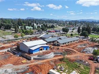 An aerial view to the North East showing the multi-purose room and 3 classroom wings with metal roofing and wood siding with a large concrete ramp and dirt pathways