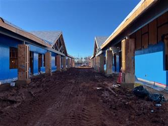 a dirt pathway between two buildings, both in the framing stage.