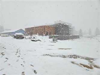 a large building made of wood and CMU block under construction in an open field with heavy falling snow