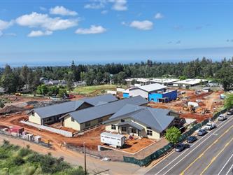 Aerial view to the South West showing the 3 classroom wings with metal roofing and installed siding with the cafeteria in the background surrounded by dirt