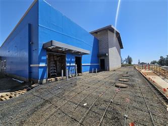 the multi-purpose room covered in blue sealer attached to the CMU block cafeteria surrounded by gravel and rebar