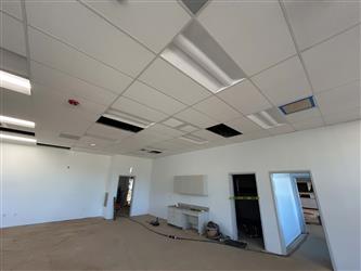 a classroom interior with finished white walls and suspended ceiling with light fixtures and missing panels