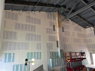 The interior of the multipurpose room with a large wall drywalled and taped