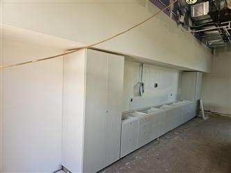 New teaching wall casework being installed in a classroom covered in drywall with exposed ventilation
