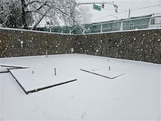 a concrete pad with large retaining wall in the background burried under a few inches of fresh snow
