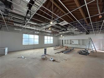 A large open classroom with drywall installed and taping in progress and exposed t-bar ceiling