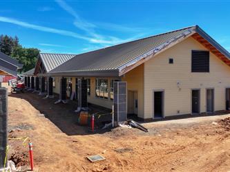 A view of Building D with the roofing and siding installed and work beginning on columns supporting the awning. Surrounded by dirt