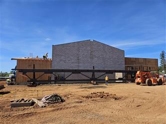 a large CMU block building with wood framed walls coming out of either side and a large steel truss sitting on the ground